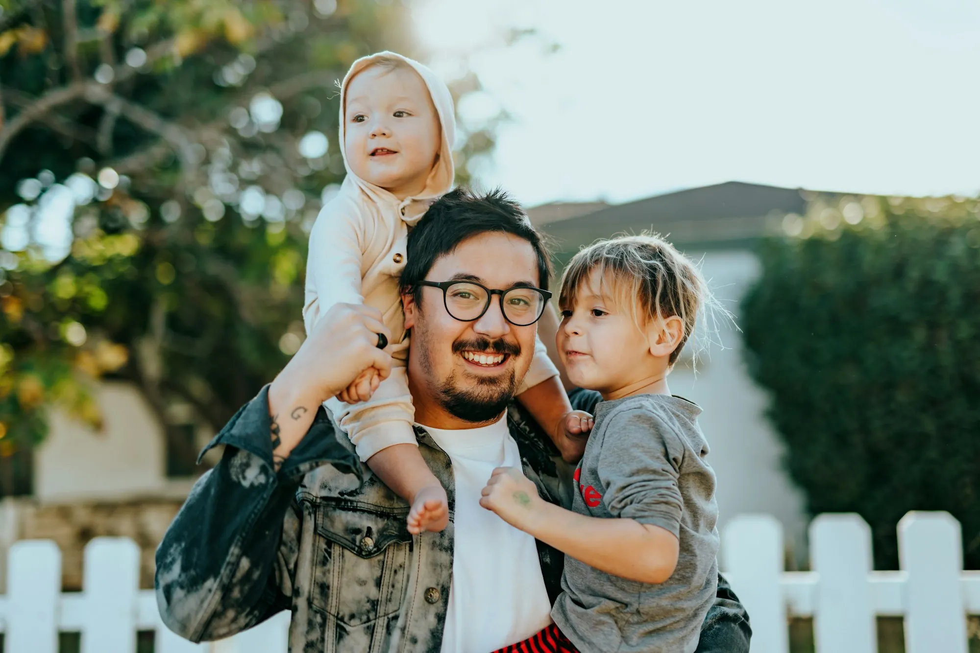 Father carrying a toddler on his shoulders beside a white picket fence